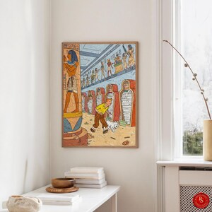 May include: Framed art print depicting a cartoon scene of a character in a yellow shirt and brown trousers, with a white dog, in an ancient Egyptian tomb. The artwork includes hieroglyphs and mummies.