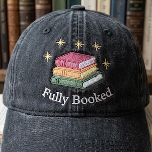 May include: A black baseball cap with an embroidered design of three stacked books in pink, orange, and green, with gold stars and the text "Fully Booked" in white. The cap is made of a soft, worn fabric.