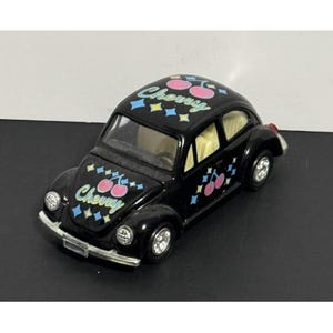 Peut inclure: Une voiture miniature noire au corps arrondi, dotée de roues argentées et d'un intérieur clair. L'extérieur est orné de motifs de cerises roses, du mot Cherry écrit en bleu clair et de petits accents en forme de losanges bleus et jaunes.
