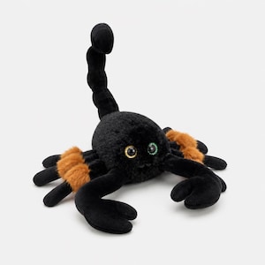May include: A plush scorpion toy featuring soft black fur, a segmented upright tail, and two large front pincers. The creature has eight legs with patches of brown fur near the joints and two large, round, glossy eyes with gold and green accents.
