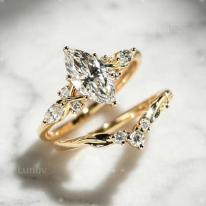 Peut inclure: Un ensemble de bagues en or composé d'une bague de fiançailles avec une pierre centrale taille marquise et d'une alliance assortie en forme de V. Les deux bagues présentent de petites pierres rondes et marquise serties sur l'or poli.