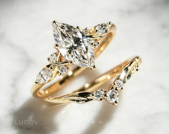 May include: A gold ring set consisting of a marquise-cut center stone engagement ring and a matching V-shaped band. Both rings feature small round and marquise-cut accent stones set along the polished gold bands, creating a cohesive design.