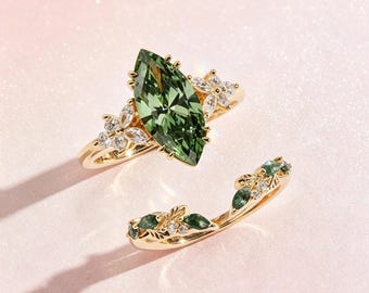 May include: A gold ring set featuring a large marquise-cut green gemstone as the centerpiece, flanked by small clear stones arranged in floral patterns. A matching curved band with leaf-shaped green stones and clear accents completes the set.