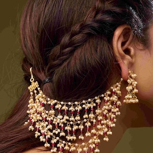 Puede incluir: Joyería para el cabello dorada y pendientes a juego. El accesorio para el cabello presenta múltiples hebras de pequeñas cuentas blancas intercaladas con cuentas rojas. Los pendientes son un grupo de cuentas similares.