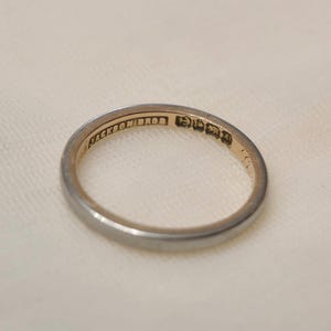 May include: A thin, circular metal ring with a smooth, polished silver-toned exterior and a gold-toned interior. The inner band is engraved with the text JACKSON BROS followed by a series of small, distinct hallmark symbols and the number 14.