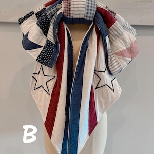 May include: A quilted scarf featuring a patchwork design in red, white, and blue. The fabric includes patterns of stripes, polka dots, and solid colors, accented with embroidered star outlines. The letter B is visible in the lower left corner.