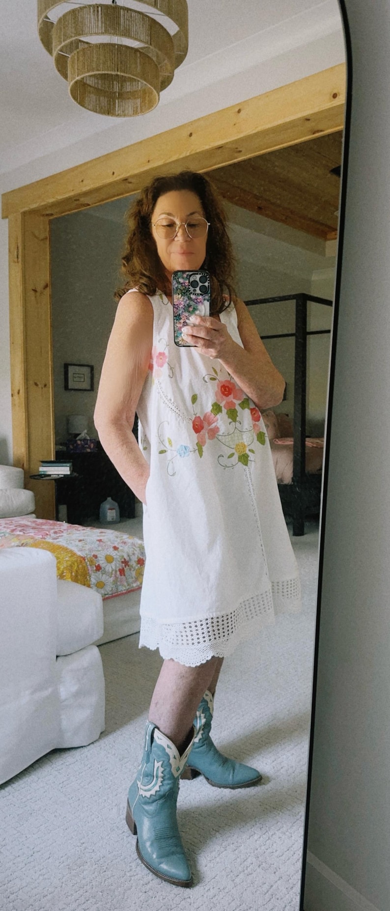 May include: White sleeveless dress with floral embroidery and a scalloped hem. The dress is paired with light blue cowboy boots.