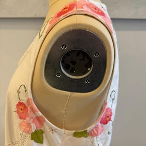 May include: Cream-colored sleeveless top with floral appliqu&eacute; details. The top features pink and red flower accents with green leaves. The straps are adorned with a floral pattern. The garment is displayed on a mannequin.