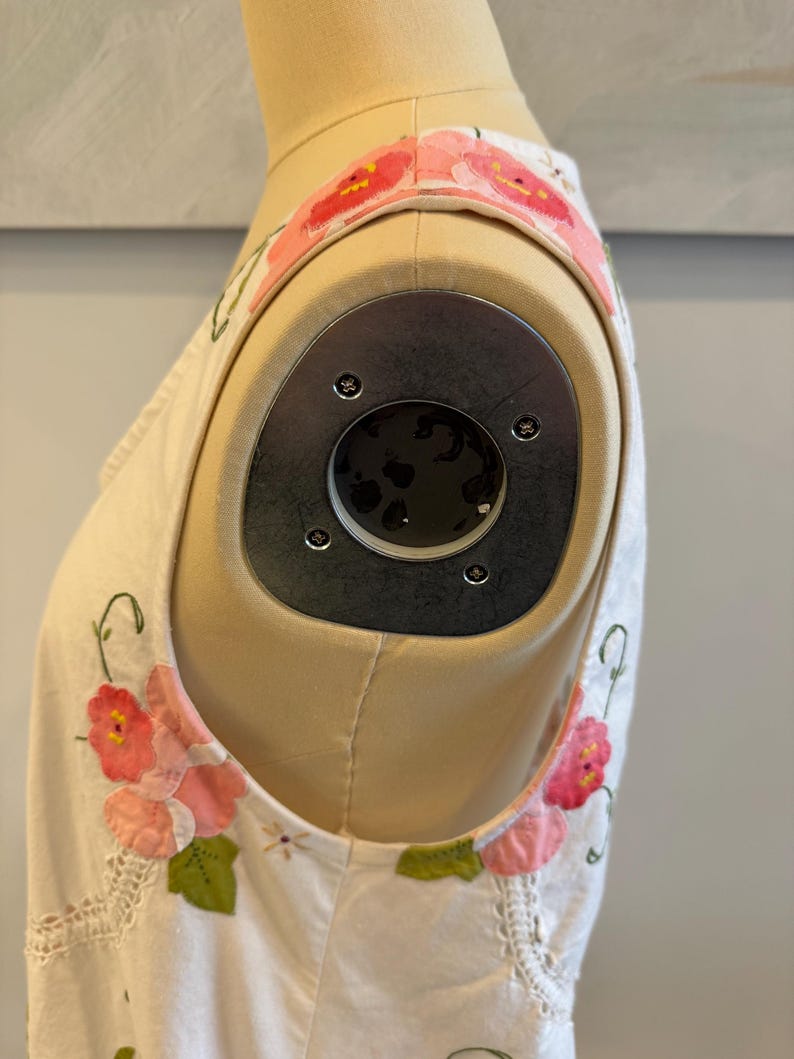 May include: Cream-colored sleeveless top with floral appliqu&eacute; details. The top features pink and red flower accents with green leaves. The straps are adorned with a floral pattern. The garment is displayed on a mannequin.