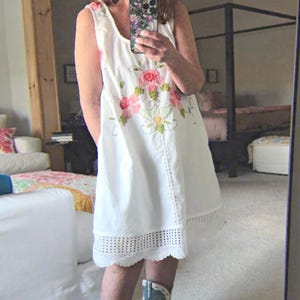 May include: White sleeveless dress with floral embroidery and a scalloped hem. The dress is paired with turquoise cowboy boots.