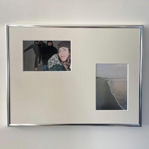 Puede incluir: Un marco de fotos rectangular de metal plateado con un paspartú blanco que tiene dos aberturas. La abertura horizontal izquierda muestra una fotografía de tres personas, mientras que la abertura vertical derecha muestra una playa de arena.