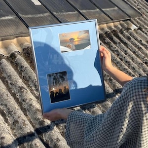 Peut inclure: Un cadre photo rectangulaire argenté avec un passe-partout bleu clair contenant deux photographies. La photo du haut montre un coucher de soleil sur l'océan, et celle du bas affiche la silhouette d'un groupe de personnes au soleil couchant.