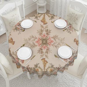 May include: A round tablecloth with a floral design in shades of beige, pink, and green. The table is set with white plates, gold-colored cutlery, and is surrounded by white chairs with floral cushions. The tablecloth has a scalloped edge.