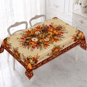 May include: A rectangular tablecloth with a cream-colored background featuring a central autumn-themed print of orange pumpkins, brown pinecones, yellow sunflowers, and multicolored fall leaves. The border has a dark red decorative pattern.