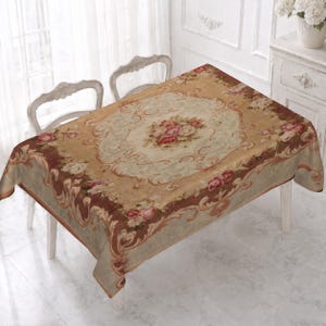 May include: A rectangular tablecloth featuring a central bouquet of pink and white roses surrounded by ornate scrollwork and floral borders in shades of tan, brown, and cream. The fabric displays a detailed pattern with intricate decorative motifs.