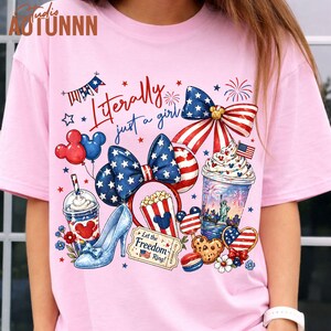 May include: Pink t-shirt with a patriotic design featuring a bow, high heel, and various American-themed graphics. The text "Literally just a girl" is displayed in red script. Includes Mickey Mouse balloons and popcorn.