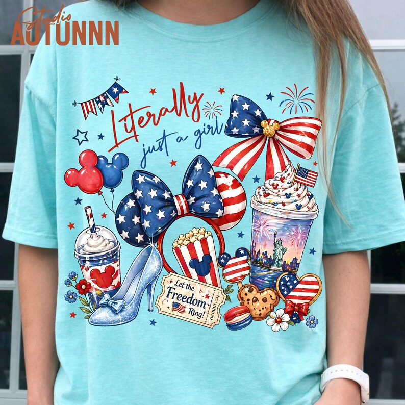 May include: Light blue t-shirt with a patriotic design featuring a bow, Mickey Mouse ears, and a high heel. The shirt includes the text "Literally just a girl" and various American flag-themed graphics.