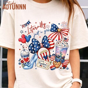 May include: Cream-colored t-shirt featuring a patriotic design with the text "Literally just a girl." The design includes a bow, Mickey Mouse balloons, a high heel, popcorn, and a beverage, all in red, white, and blue.