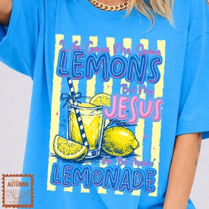 Può includere: T-shirt azzurra con un design grafico. Il design presenta il testo "Life Gave Me Some Lemons But My Jesus Made Lemonade". Include un bicchiere di limonata, fette di limone e un limone intero. La maglietta ha un girocollo.