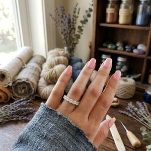 May include: A silver-toned ring featuring a continuous band of round, clear, faceted stones worn on a finger. The ring has a polished metal setting that holds each stone securely in place, creating a uniform, sparkling appearance across the band.