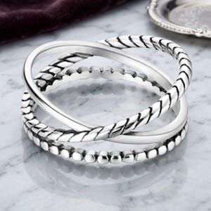 May include: A silver ring featuring three interlocking bands. One band has a smooth polished finish, the second band displays a twisted rope texture, and the third band is composed of a series of small, uniform silver beads arranged in a row.