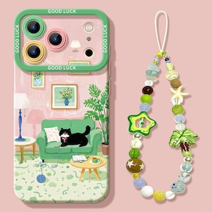Peut inclure: Coque de téléphone avec bordure verte et inscription "GOOD LUCK" répétée. L'étui présente une illustration fantaisiste d'un salon avec un chat noir sur un canapé vert. Un charm en perles avec des accents d'étoiles et de palmiers est suspendu.