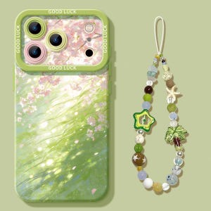 May include: A green phone case with a floral design and the words "GOOD LUCK" in white. A beaded phone charm with a star, palm tree, and seashell accents hangs next to the case. The case has a green border around the camera.