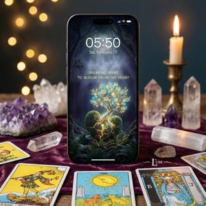 May include: A smartphone displays a digital art piece with a tree growing from a heart, surrounded by crystals, tarot cards, and a lit candle. The screen shows the time 05:50 and the date, February 21, with the text "BREAKING APART TO BLOOM FROM THE HEART."
