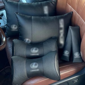 Puede incluir: Un conjunto de accesorios automotrices negros que incluye dos almohadas rectangulares, dos almohadas para el cuello contorneadas más pequeñas y dos fundas para cinturones de seguridad, con acabado de cuero sintético negro.