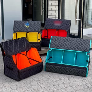 May include: Four rectangular car trunk organizers with black quilted exterior panels. Each organizer features a folding lid and interior compartments in bright yellow, red, neon orange, and turquoise. One organizer displays a blue and yellow trident emblem.