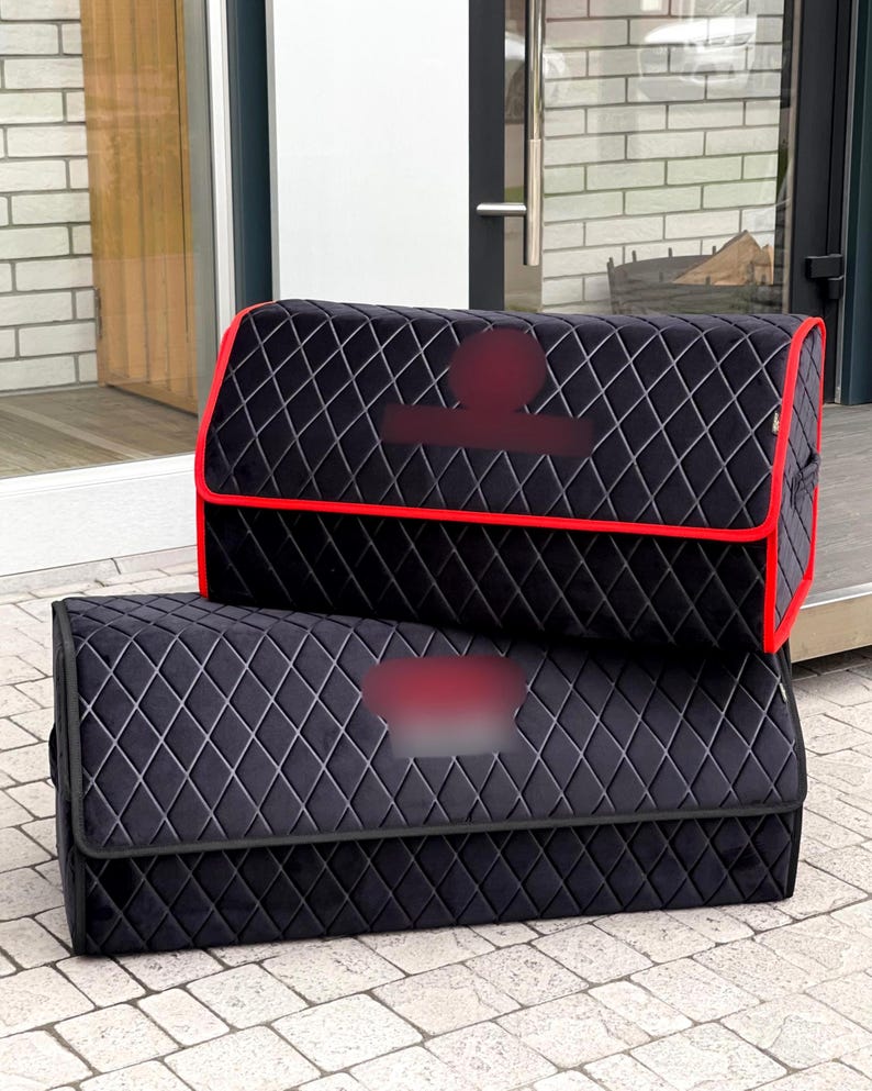 May include: Two black car trunk organizers with a diamond pattern. The top organizer has a red trim. The organizers are made of a soft material and are designed to keep the car trunk organized.