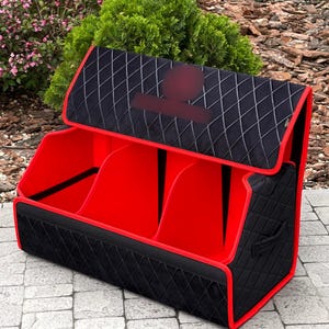 May include: A black and red storage organizer with three compartments. The exterior is black with a diamond pattern, and the edges are trimmed in red. The interior is bright red. The organizer has a handle on the side and a hinged lid.