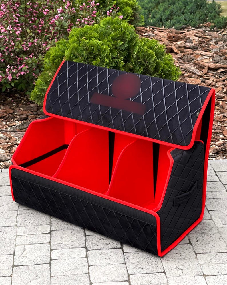 May include: A black and red storage organizer with three compartments. The exterior is black with a diamond pattern, and the edges are trimmed in red. The interior is bright red. The organizer has a handle on the side and a hinged lid.