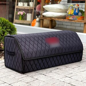 May include: A black, quilted storage container with a diamond pattern. The container has a rectangular shape with a curved top and a handle on the side. The background includes a wooden shelf with decorative items.