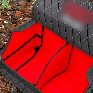 May include: Black car organizer with a quilted diamond pattern on the exterior. The interior is bright red and divided into multiple compartments. The organizer is designed to keep items secure and organized in a vehicle.