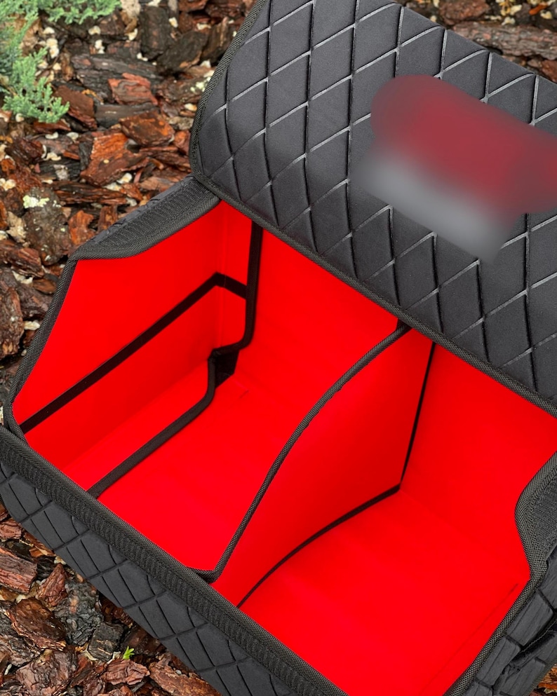 May include: Black car organizer with a quilted diamond pattern on the exterior. The interior is bright red and divided into multiple compartments. The organizer is designed to keep items secure and organized in a vehicle.