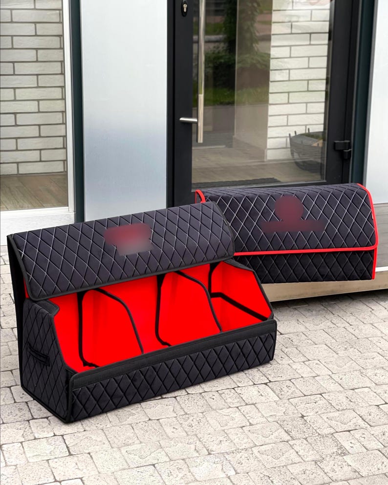 May include: Two black quilted car organizers with red interiors. The organizers have a diamond pattern and are designed to store items in a vehicle. One organizer is open, revealing the red interior.