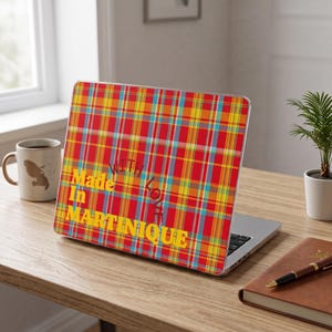 Peut inclure: Un autocollant pour ordinateur portable avec un motif à carreaux rouge, jaune et bleu vif. Le texte "Made In MARTINIQUE" est imprimé en lettres jaunes grasses en bas à gauche, avec les mots "WITH LOVE" arqués en couleur sombre au-dessus.