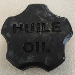 May include: Black oil cap with the word "HUILE" above "OIL" in bold, raised lettering. The cap has a geometric pattern and a unique, star-like shape.