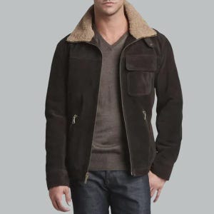 May include: A dark brown suede jacket featuring a tan faux-shearling collar, a full-length front zipper, and two zippered waist pockets. The jacket includes a single chest pocket with a flap closure and is worn over a brown V-neck sweater and jeans.