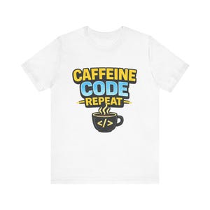 Op de afbeelding: Wit t-shirt met de tekst "CAFFEINE CODE REPEAT" in geel en blauw, met een koffiekopje met codesymbolen. Het ontwerp staat in het midden van de voorkant van het shirt, voor programmeurs en koffieliefhebbers.