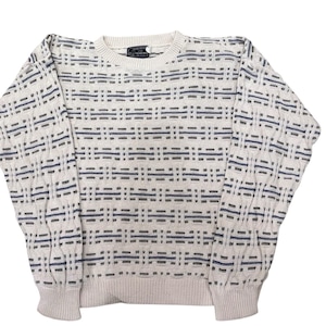 May include: Cream-colored sweater with a geometric pattern in navy and gray. The long-sleeved knitwear features a crew neck and ribbed cuffs and hem. A small label is visible near the neckline. The sweater is a classic piece of apparel.