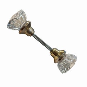 May include: A pair of clear, faceted glass door knobs connected by a central metal spindle. Each knob features a fluted, starburst-like pattern and is mounted on a polished brass-toned metal base, creating a classic hardware assembly.