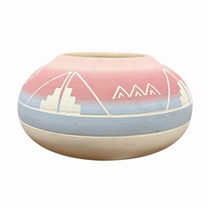 Può includere: Un vaso in ceramica rotondo con finitura opaca e una sfumatura di colore che passa dal rosa tenue in alto all'azzurro al centro e al crema alla base. La superficie è decorata con motivi geometrici bianchi incisi sul corpo del vaso.