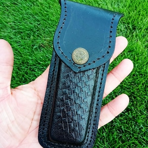 May include: Black leather knife sheath with a basket weave pattern and a brass button. The sheath has a stitched border and the text "X - 640" in the upper left corner.