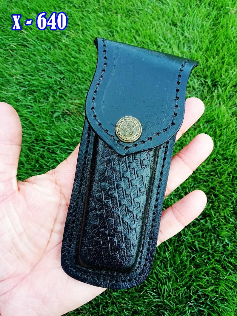 May include: Black leather knife sheath with a basket weave pattern and a brass button. The sheath has a stitched border and the text "X - 640" in the upper left corner.