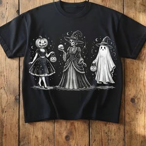 Könnte beinhalten: Ein schwarzes Kurzarm-T-Shirt mit einer weißen grafischen Illustration von drei Figuren: eine Person mit Kürbiskopf, ein Skelett in einem Hexenhut und Kleid, das einen Schädel hält, und ein Geist mit Hexenhut, der einen Trick-or-Treat-Eimer hält.