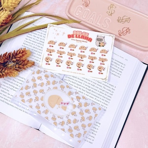 May include: A clear plastic card holder with a pattern of small yellow mushrooms and a cartoon mushroom illustration. A sticker sheet with the text "DULCE DE LLAMA" and illustrations of smiling cookies is also visible.