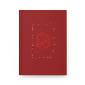 May include: A red journal featuring a stack of heart-shaped biscuits within a dotted border. Each biscuit has a heart design. The journal has a solid red cover.