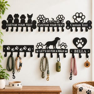 May include: Six black metal wall-mounted leash and accessory holders featuring various designs including dog silhouettes, paw prints, and heart shapes. Some racks display text such as CUSTOM YOUR TEXT, Daxton, LET'S GO FOR A WALK, and BELLA with hooks.